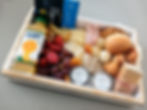 Caixa de café da manhã com queijos, presunto, frutas frescas, pães, waffles, suco e café, organizada