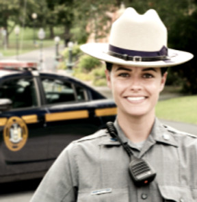 Smiling female state trooper in uniform by patrol vehicle.