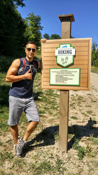 A man giving the thumbs up beside a hiking trail sign at Blue Mountain Ontario.
