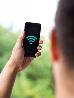 A man holding a mobile phone outdoors with a wifi icon on the screen.