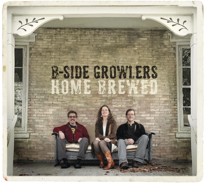 Photo of three band members sitting on a coach on a porch in front of a brick building. The words B-side Growlers, Home Brewed are painted on the brick behind them.