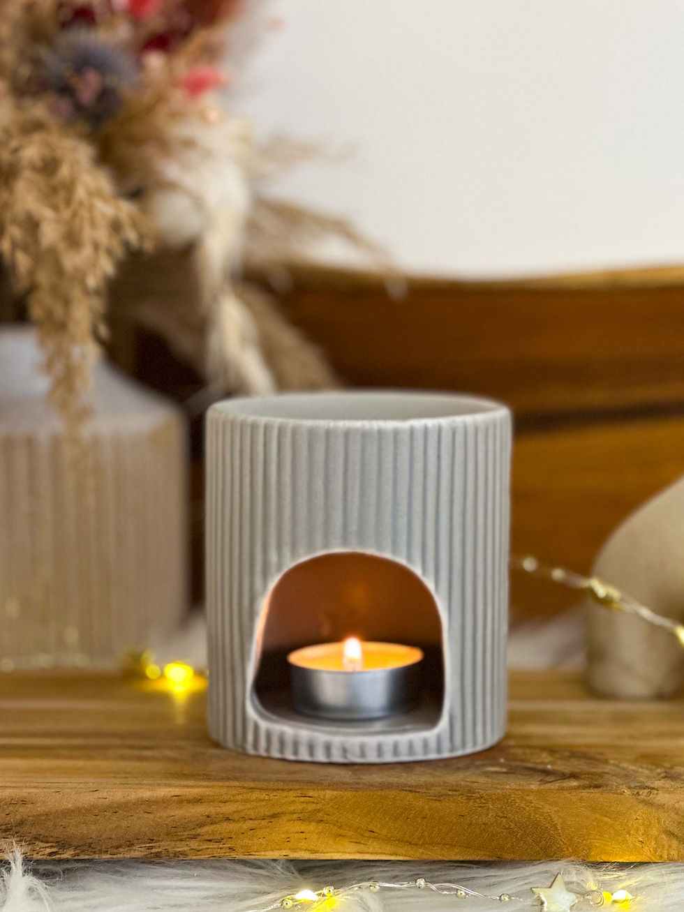 Diffuseur de parfum céramique gris cannelé, bougie allumée, fond floral.