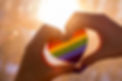 Two hands are curved in the shape of a heart around a rainbow heart sticker.