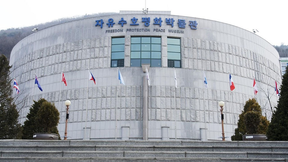 Gray stone museum with "Freedom Protection Peace" sign. Flags line the entrance. Trees and steps create a formal atmosphere.