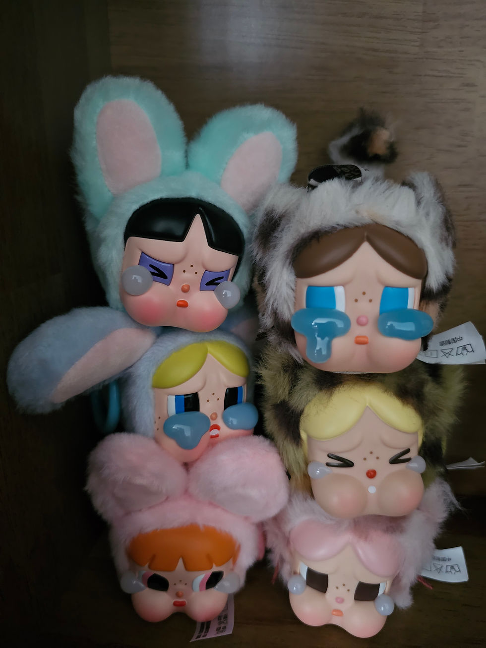 Colorful doll figures dressed in animal costumes with various sad expressions, stacked on a wooden shelf. Tags with symbols are visible.