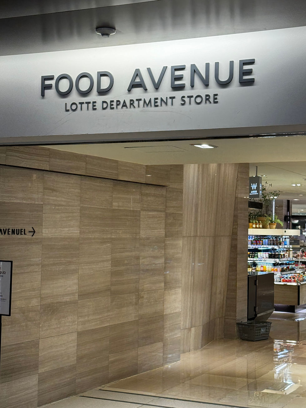 Entrance to "Food Avenue" at Lotte Department Store, with shiny beige walls. Visible shelves of snacks and drinks in the background.