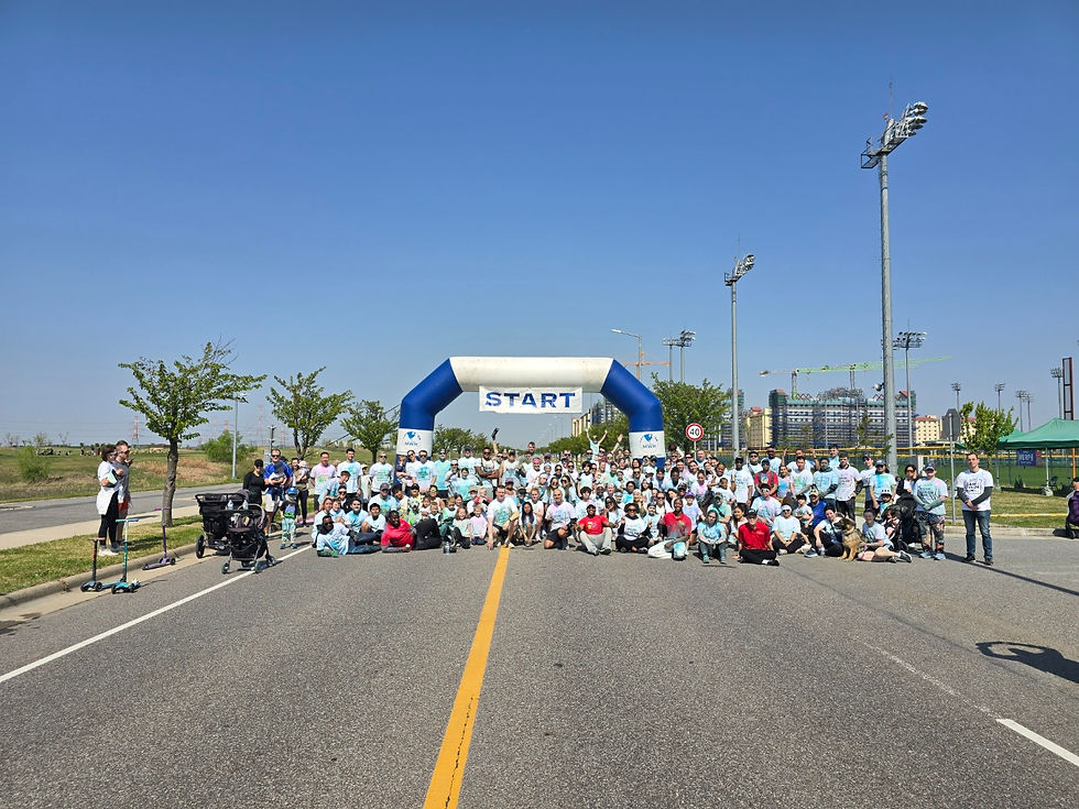 A large group gathers under a "START" arch on a sunny road, with trees and buildings in the background. People wear colorful shirts.