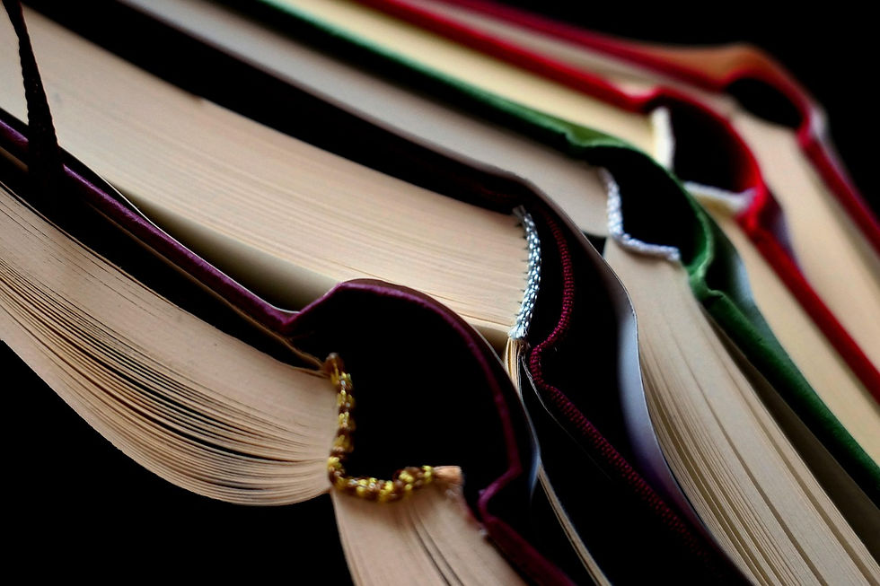 Books with colorful ribbons and edges are stacked at angles, showcasing pages and covers. The background is dark, adding contrast.