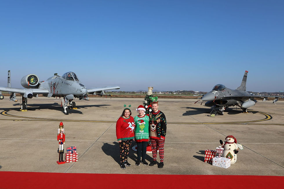 Three people in festive attire stand between two military jets on a runway. Christmas decorations, gifts, and a nutcracker are displayed nearby.