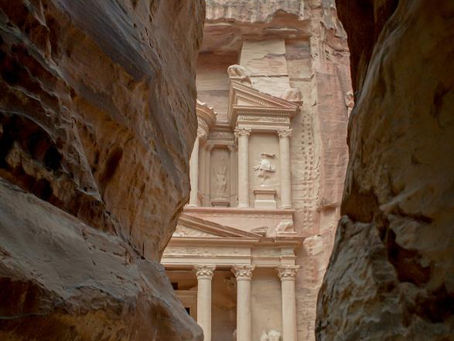 Ancient rock-carved facade of Petra's Treasury framed by narrow canyon walls, with earthy tones and an air of mystery.
