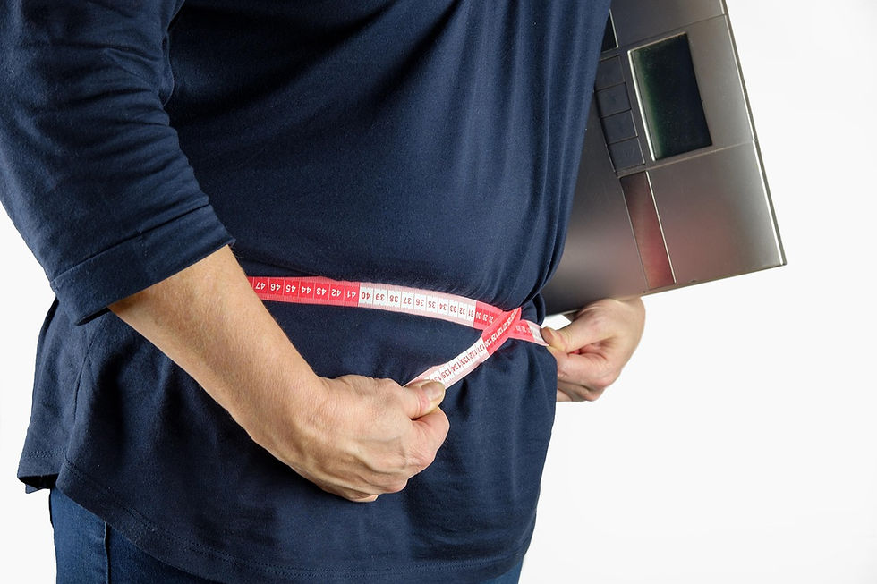 Person in a blue shirt measures waist with a red tape, holding a black scale. White background. Mood appears focused.