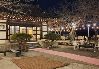 Traditional building at night with lit windows, string lights above, bare trees, and outdoor seating. Calm, cozy atmosphere.