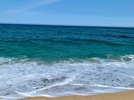 Sandy beach with gentle waves meeting the shore under a clear blue sky. The ocean is calm and vibrant, creating a tranquil atmosphere.