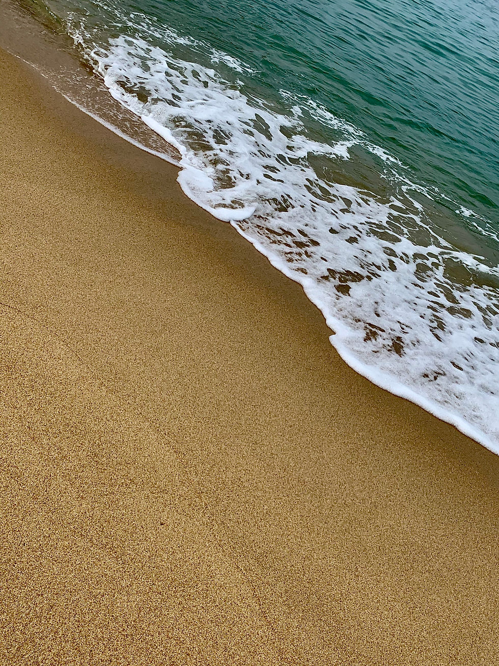 Gentle waves with white foam wash onto a sandy beach. The ocean is deep turquoise, evoking a calm, serene atmosphere. No people present.