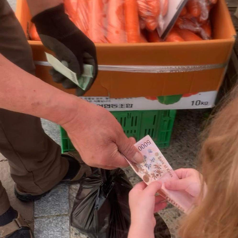 Hands exchanging a 5,000 Korean won bill by a box of carrots in a market setting. Mood is transactional with focus on money exchange.