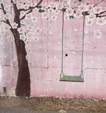 A painted swing and cherry blossoms on a pink wall create a serene and artistic scene. No text visible.