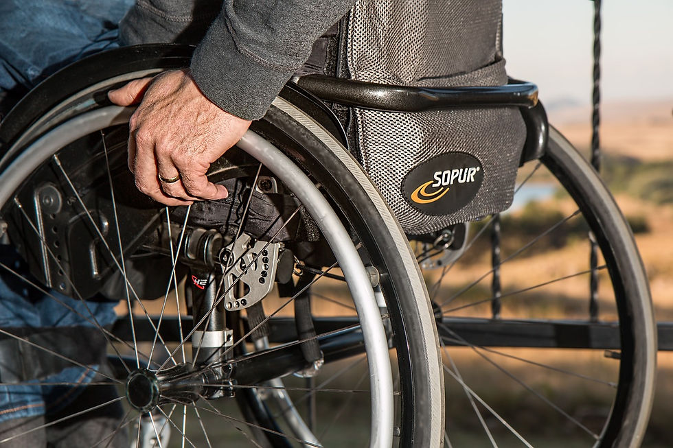 Hand gripping a wheelchair wheel with "Sopur" logo. Outdoor setting, blurred background. The person wears a grey sleeve and a gold ring.