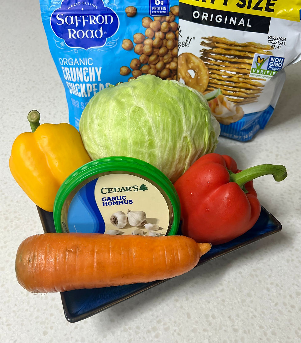 Veggies, garlic hummus in a bowl with chips and chickpeas. Yellow pepper, red pepper, carrot, lettuce on a kitchen counter.