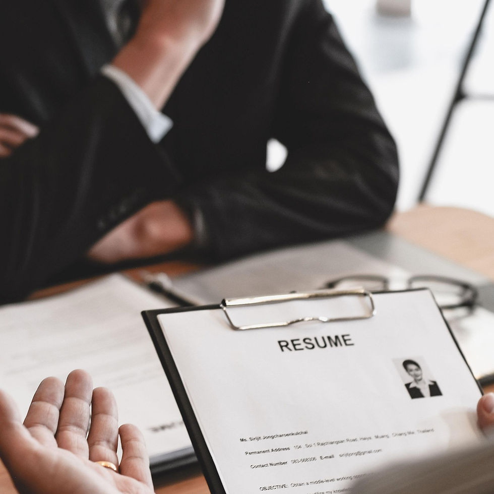Person holding a resume in foreground, another person sits thoughtfully with a hand on chin in blurred background. Job interview setting.