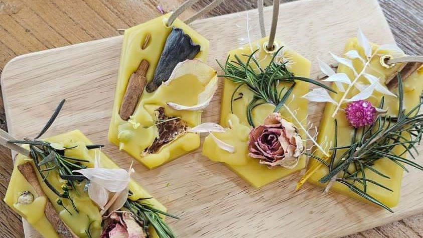 Yellow wax sachets on a wooden board, decorated with dried flowers, herbs, and spices. Warm, rustic feel with vibrant natural elements.
