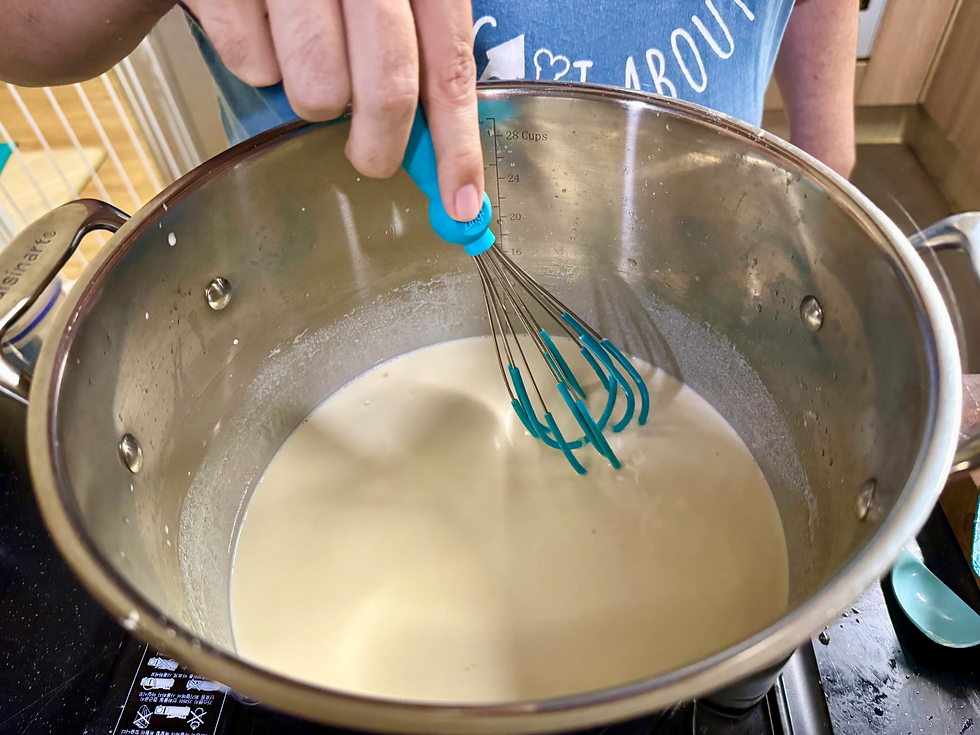 a hand with a whisk stirring a creamy substance in a stainless steel pot