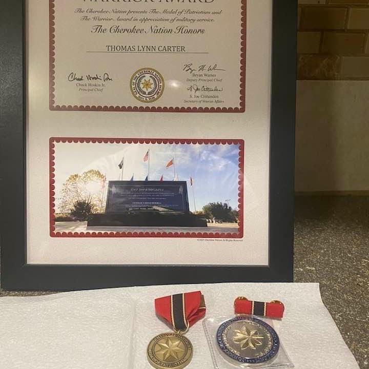 Framed certificate honoring Thomas Lynn Carter with a monument photo. Two medals with red ribbons lie below on a white cloth.