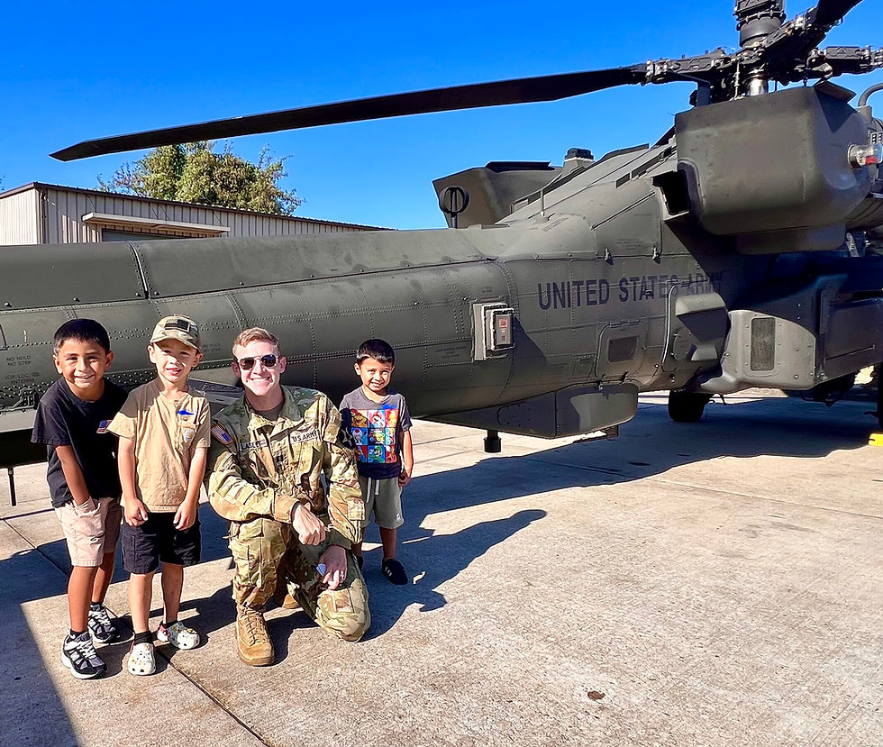Soldier with three smiling kids in front of a U.S. Army helicopter on a sunny day. Helicopter marked "UNITED STATES ARMY" in black.