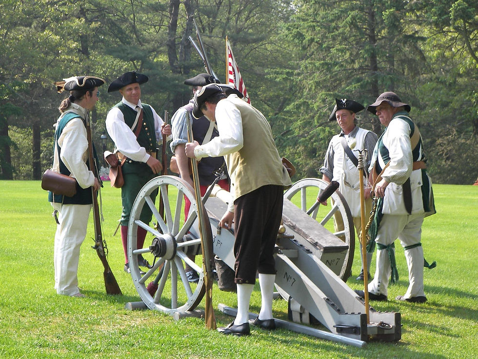 Reenactors in historical attire gather around a cannon on a grassy field with trees in the background, displaying focus and engagement.