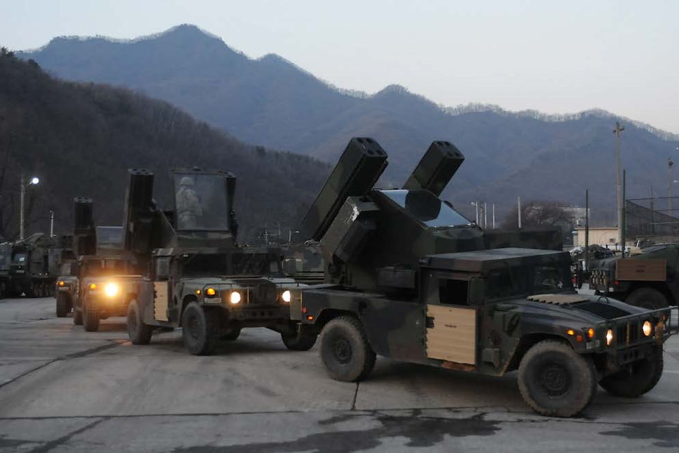 Military vehicles with mounted launchers drive on a base with mountains in the background. It's dusk, and headlights create a somber mood.
