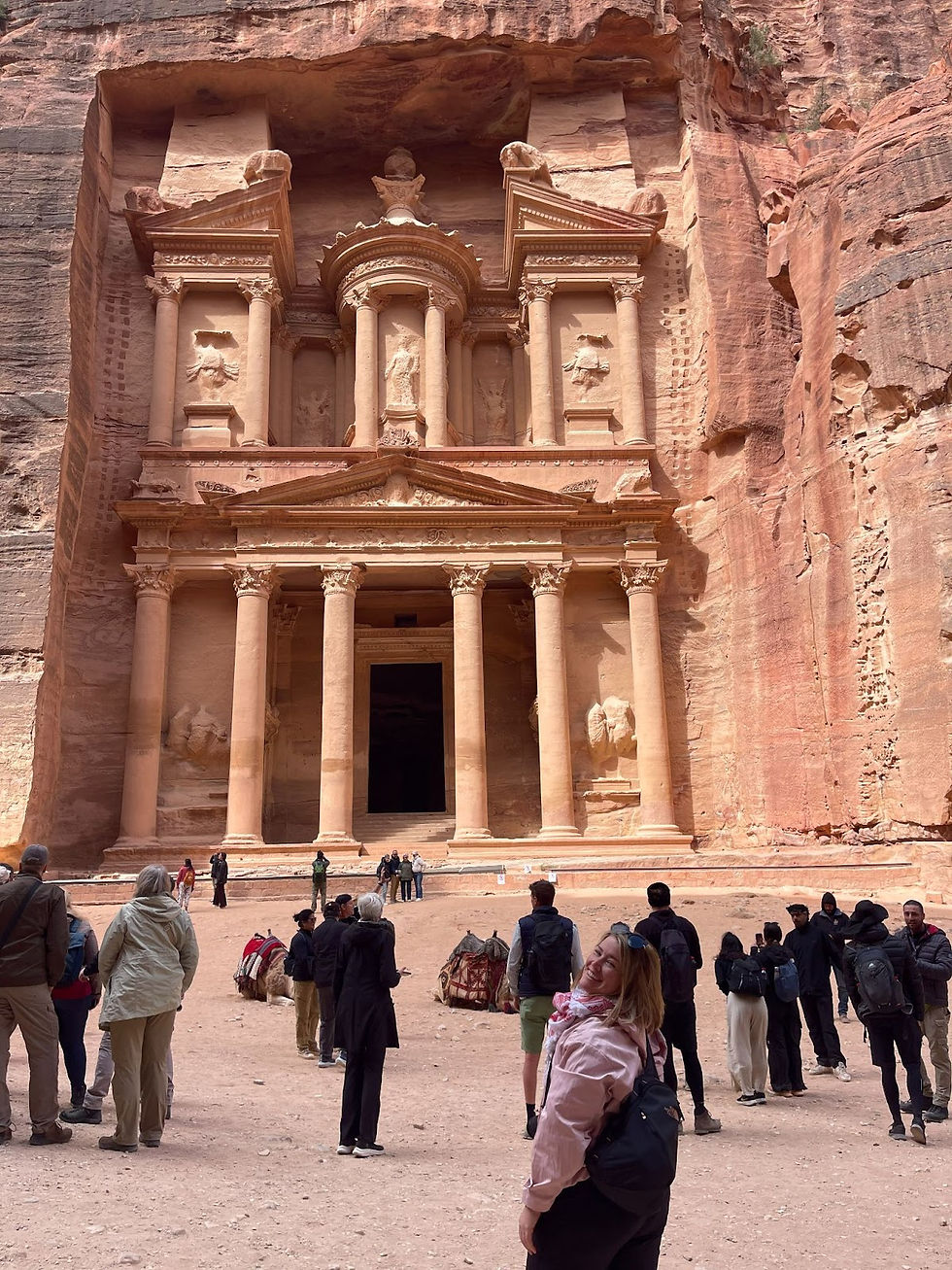 Tourists admire the ancient rock-carved facade in Petra, Jordan. The warm sandstone hues dominate the majestic background.