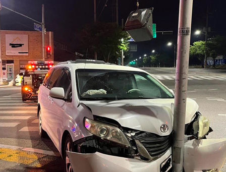 White minivan crashed into a traffic signal pole at night; red light above. No visible people. Urban setting. Minor front damage.