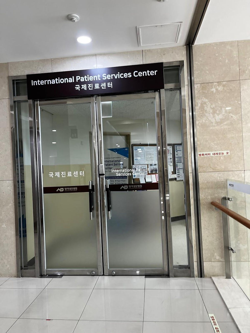 Glass doors labeled "International Patient Services Center" in a tiled hallway. Signs with Korean text visible. Bright, clean setting.