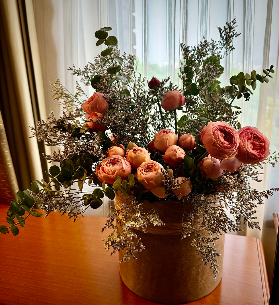 Bouquet of pink roses and greenery in a brown vase on a wooden table. Sheer curtains in the background add a soft, elegant touch.