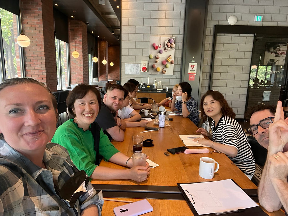 Smiling group of seven people at a wooden table in a modern café, with drinks and papers, brick walls, and artwork in the background.