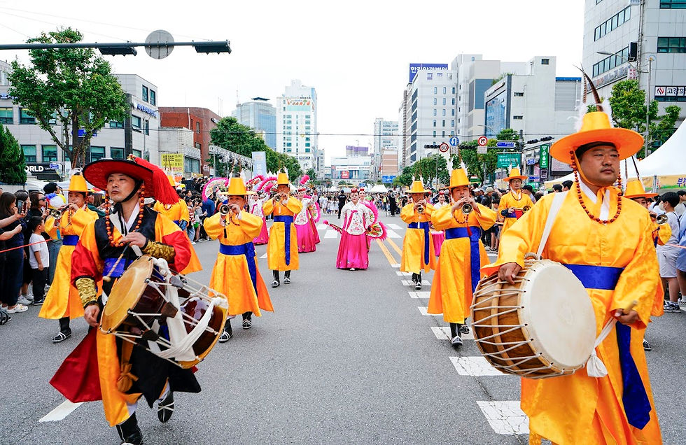 Marching band in vibrant yellow and blue traditional attire plays instruments on a city street, surrounded by onlookers and tall buildings.