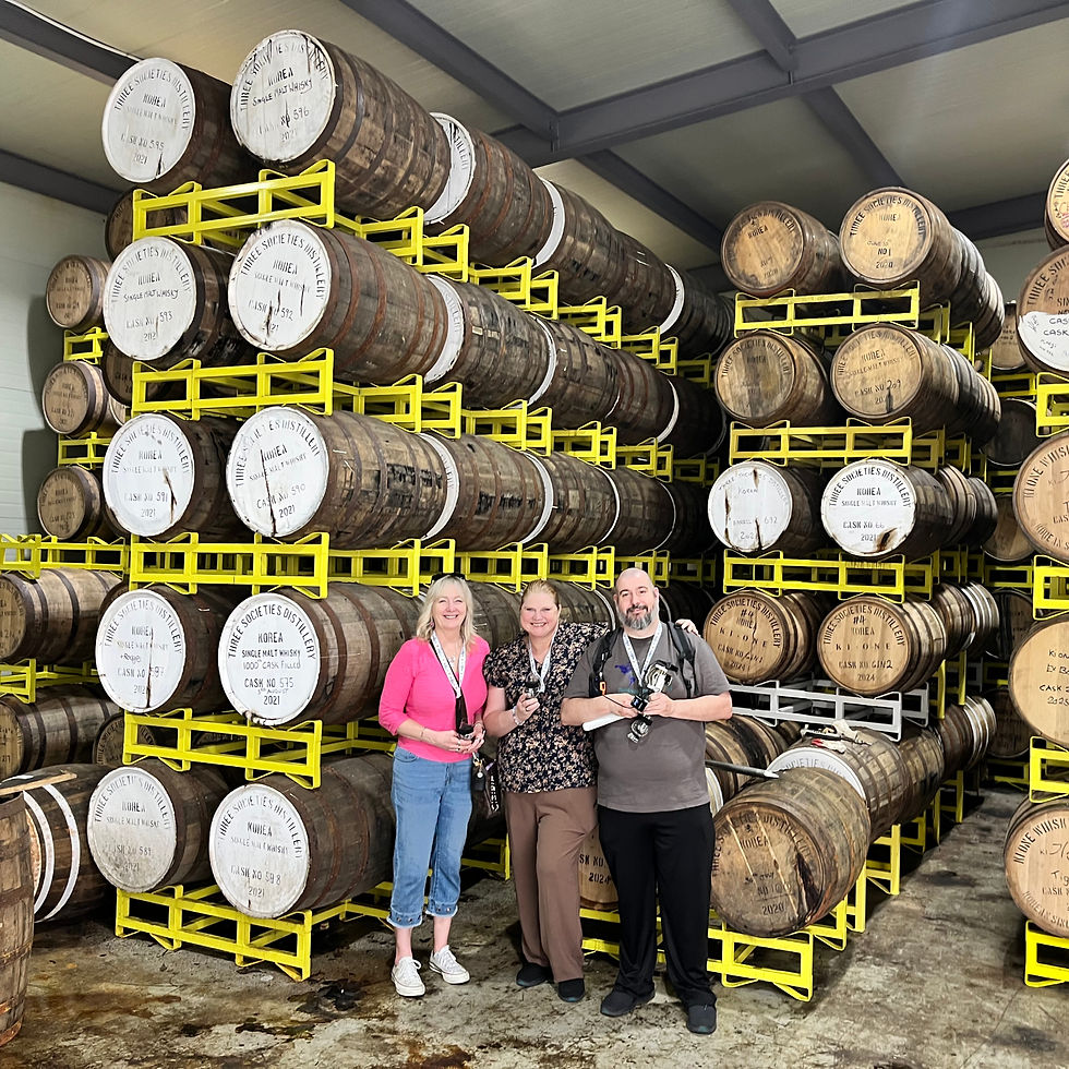 three people standing in front of barrels stamped ki one distillery and three societies distillery