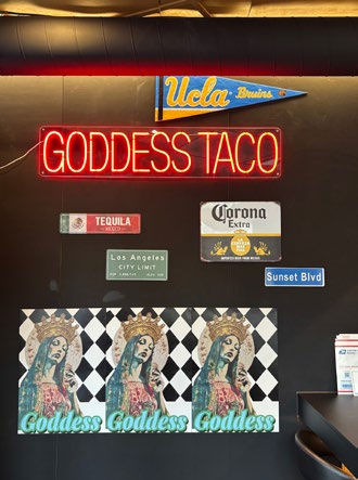 Neon signs read "GODDESS TACO" with various street-style signs below. Artistic "Goddess" images and vibrant colors create a lively vibe.