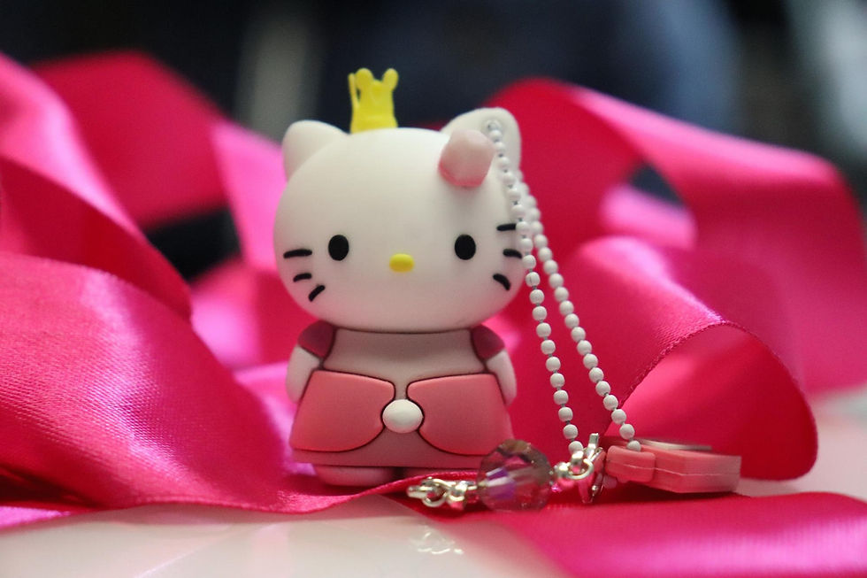 Cute Hello Kitty keychain with a crown, set against bright pink ribbon background. Beaded chain and crystal charm attached.