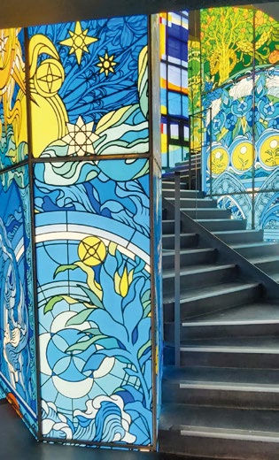 Colorful stained glass panels with star and wave designs brighten a staircase. Blue and yellow hues add a vivid, artistic atmosphere.