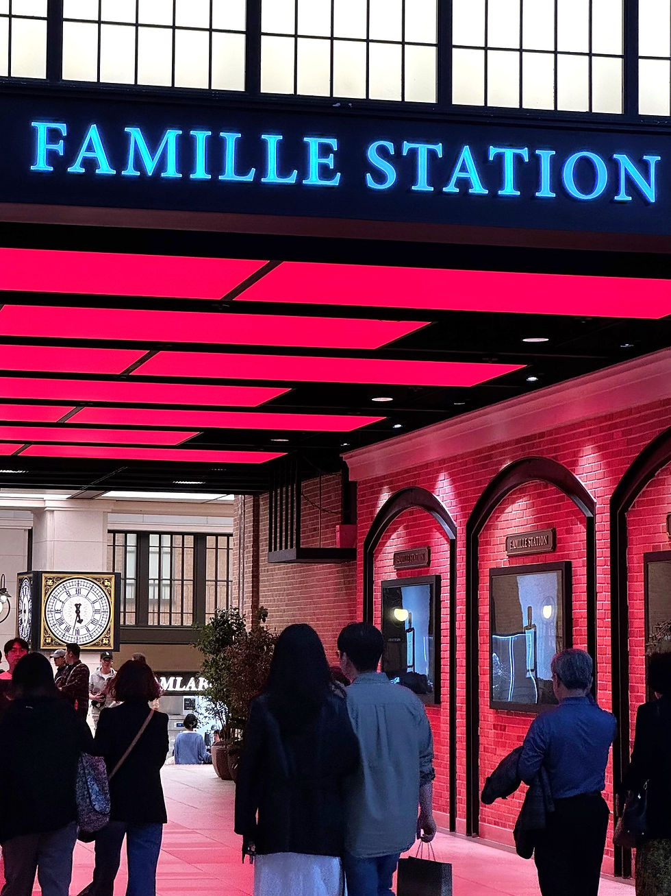 People walk under a red-lit ceiling at Famille Station. Brick walls and a large clock add to the cozy indoor setting.
