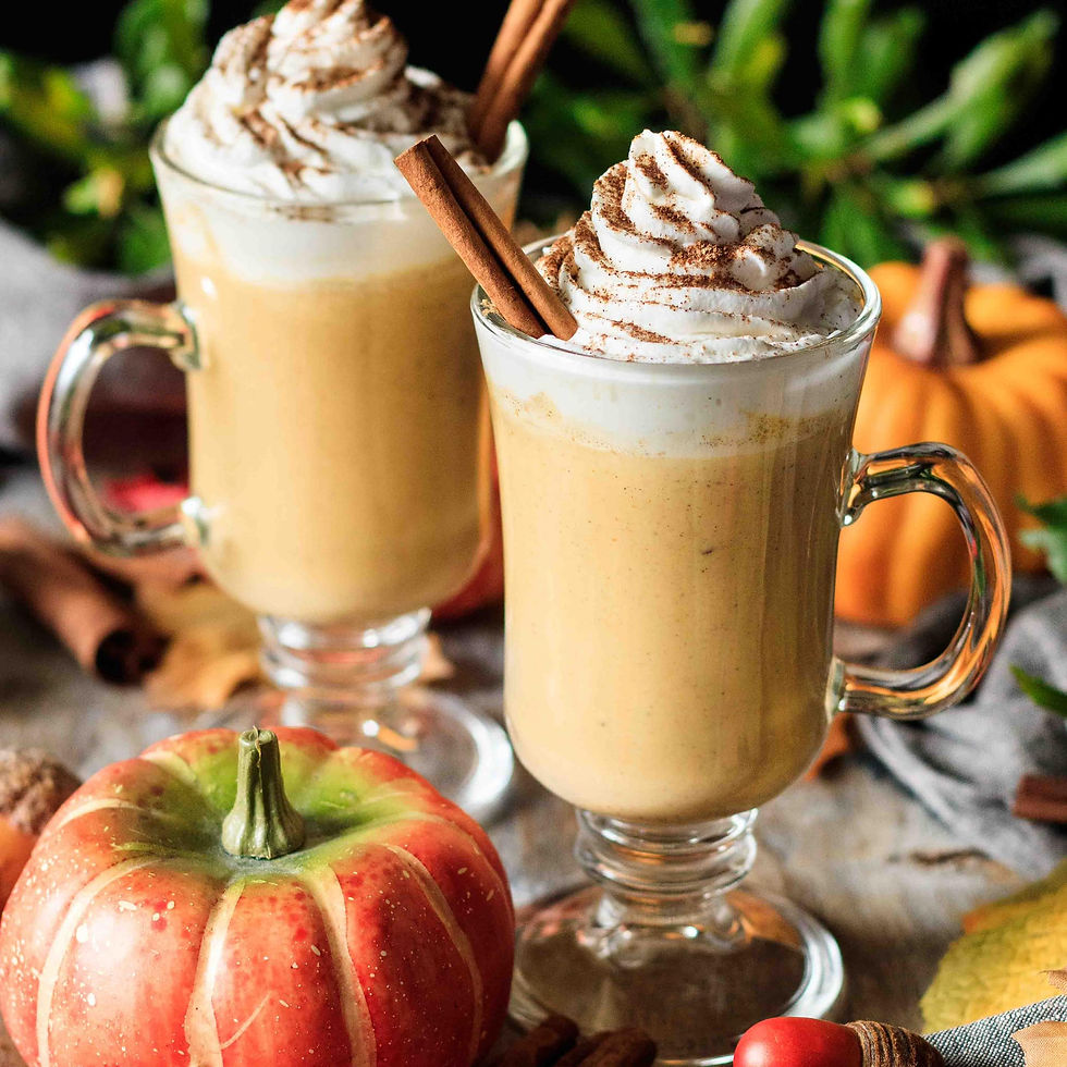 Two glass mugs of pumpkin spice latte topped with whipped cream and cinnamon sticks. Autumn decor includes pumpkins and leaves. Cozy mood.