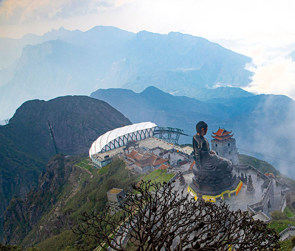 Large Buddha statue on a mountain platform, surrounded by misty, blue-hued peaks and red-roofed buildings; peaceful atmosphere.
