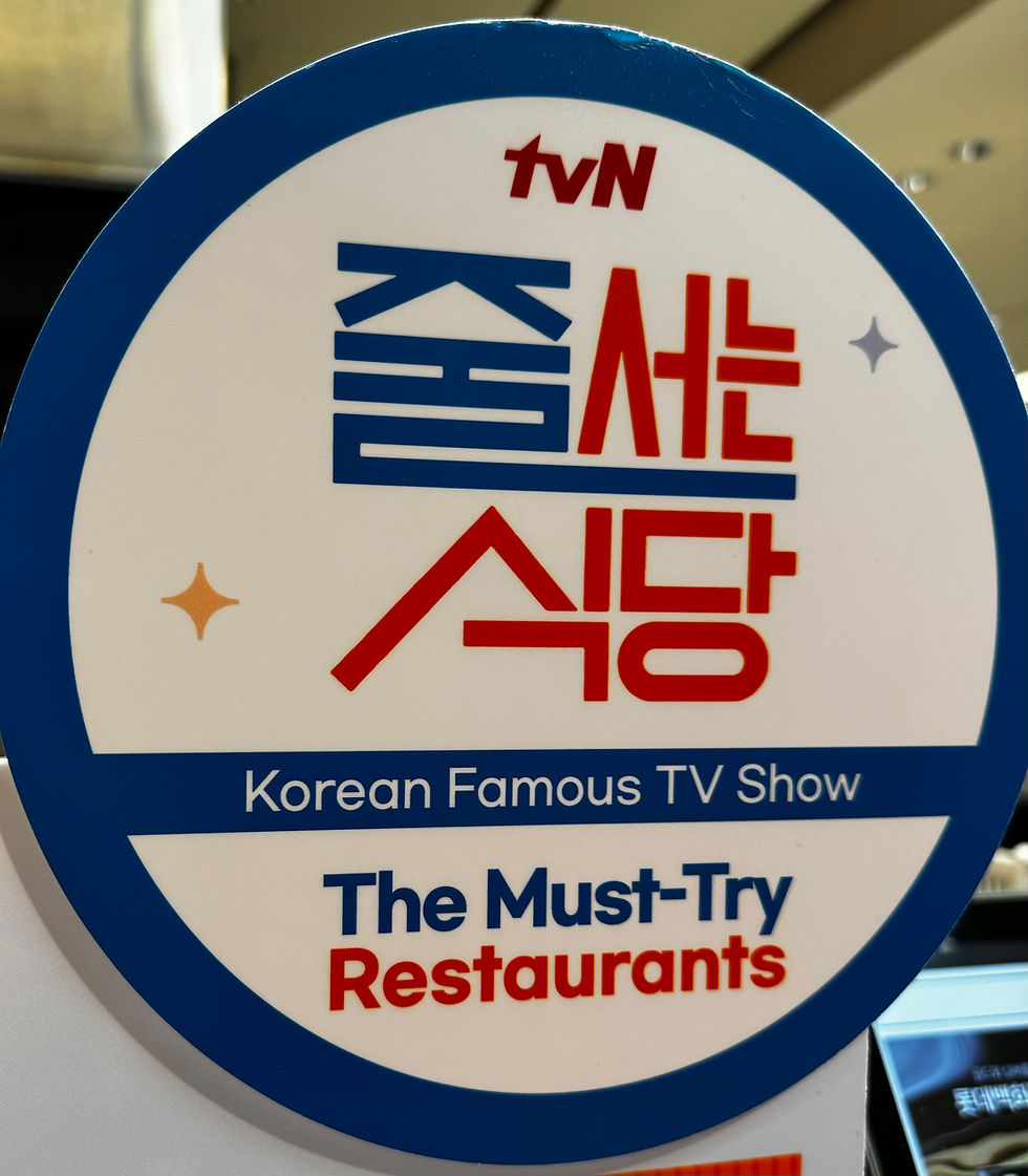 Circular sign with Korean and English text reading "Korean Famous TV Show" and "The Must-Try Restaurants" against a blue and white background.