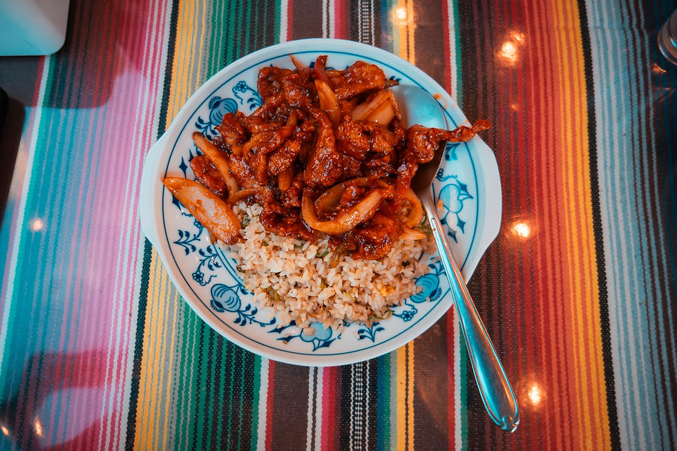 Plate of stir-fried beef and onions over rice on a blue patterned dish. Background features a colorful striped tablecloth. Reflective spoon nearby.