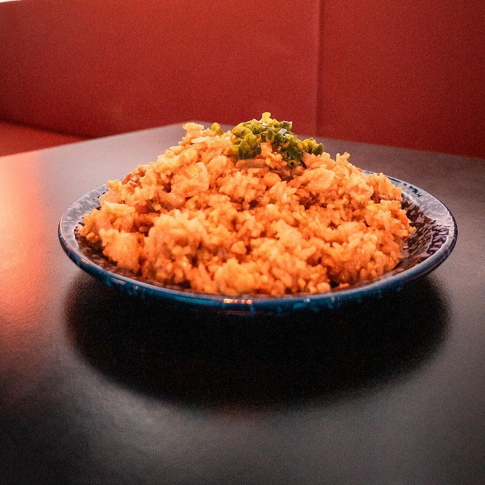A plate of golden-brown fried rice topped with chopped greens sits on a dark table, with a warm red background creating a cozy ambiance.