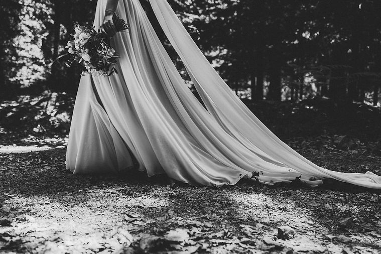Schwarz-Weiß-Fotografie eines Brautkleids mit fließendem Stoff und Blumenstrauß im Wald – Hochzeitsfotografie von Fabio Bosco
