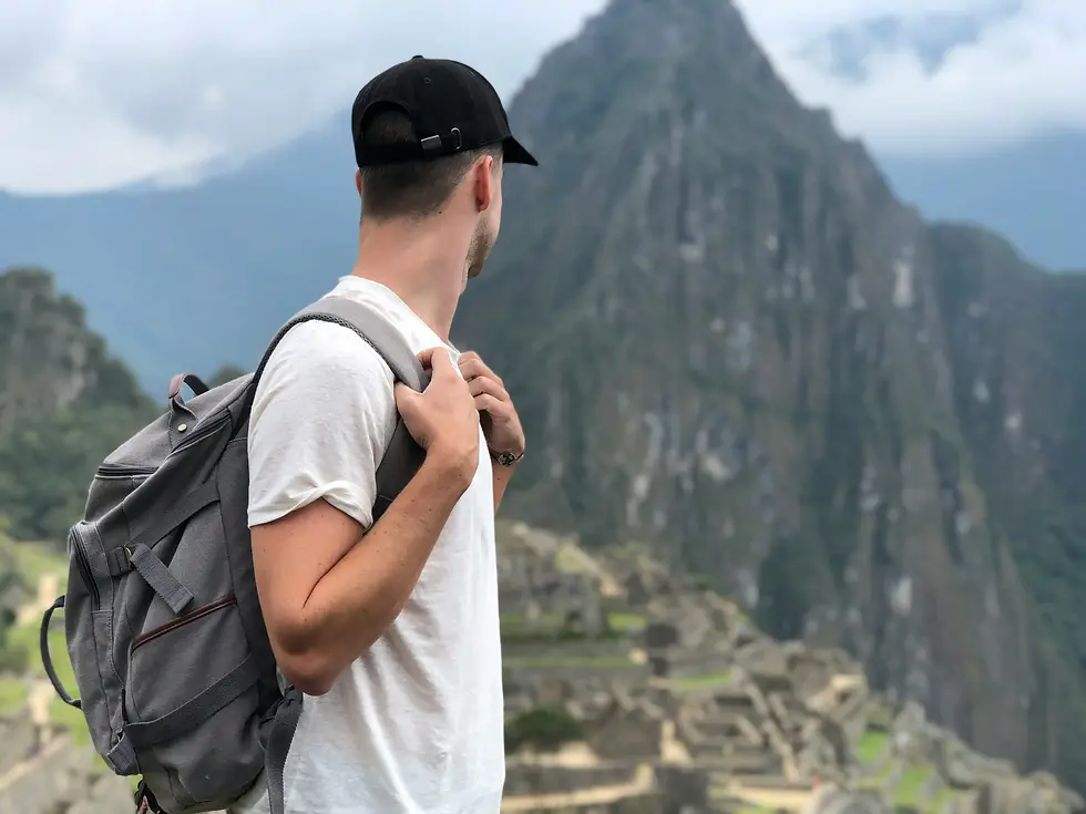 Man in a white shirt and black cap with a gray backpack looks at a mountain landscape, evoking a sense of exploration and wonder.