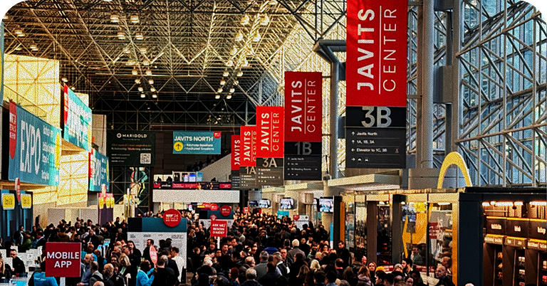 Palco principal da NRF 2026 Retail’s Big Show com telões exibindo o logotipo do evento e uma apresentação sobre inteligência artificial no varejo, enquanto palestrantes conversam em poltronas diante de uma plateia lotada em um grande auditório.