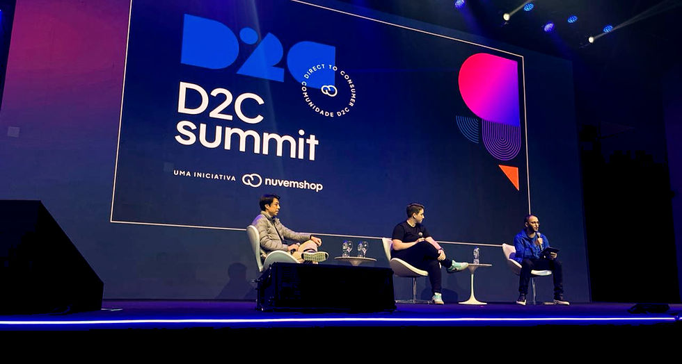 A imagem mostra um painel do D2C Summit, com três palestrantes discutindo sobre o tema "Pós-venda como uma oportunidade de fidelização". Eles estão em um palco iluminado, com uma tela de fundo exibindo o logo do evento "D2C Summit" e o texto "Uma Iniciativa Nuvemshop". O ambiente é bem iluminado, com uma configuração profissional de palco e público. O foco está na interação dos palestrantes e na apresentação de estratégias para o pós-venda no setor de e-commerce.