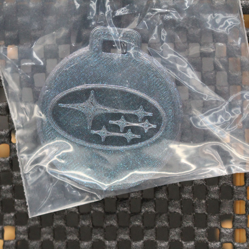 Subaru logo keychain in plastic packaging on a textured surface background.